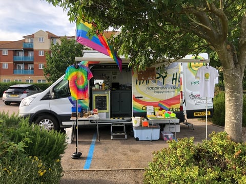 Colorful mobile food truck with rainbow decorations parked on a residential street lined with trees and brick apartments.