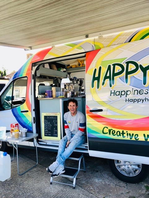Person sitting in doorway of colorful rainbow food truck with Happy Happiness branding and creative design